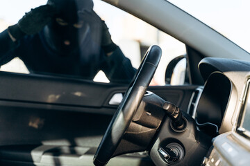 View from the car at the man dressed in black with a balaclava on his head looking at the glass of...