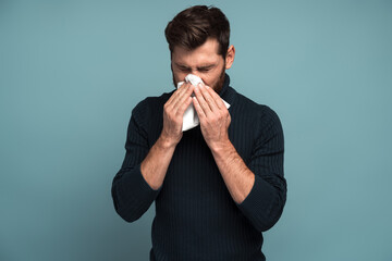 Cold and flu. Portrait of sick bearded young man standing, holding tissue on mouth and feeling...