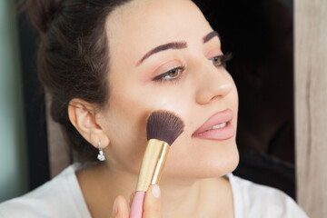 Young beautiful  woman is wearing makeup. Fashion makeup and cosmetics. Makeup brush in a woman's hand.