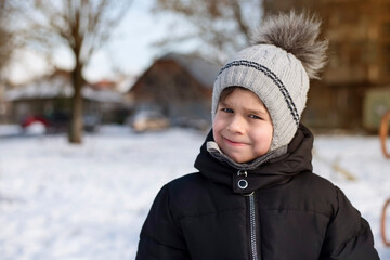 A little boy in a warm winter hat and jacket returns home in the winter from a walk, fresh air and sunlight makes the boy happy and healthy