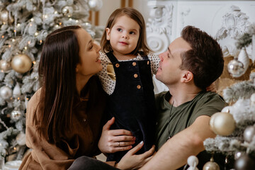 Happy dad, mom and daughter are enjoying the New Year and Christmas holidays. Dad, mom and daughter are sitting against the background of a stylishly decorated Christmas tree and enjoy the holiday