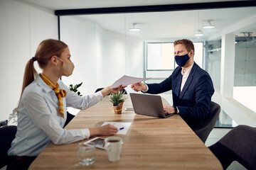 Business colleagues work on paperwork and wear face masks due to coronavirus pandemic.