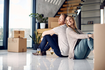 Young couple enjoys while sitting back to back on floor after moving in new apartment.