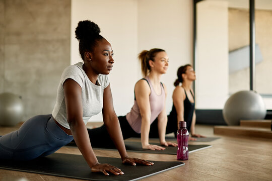 Black female athlete warms up while doing stretching exercise on group training at gym.