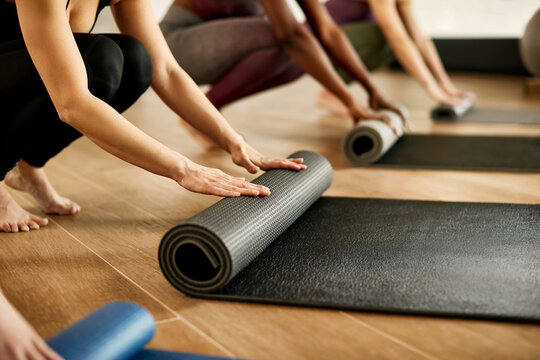 Close-up of athletic women roll their exercise mats after sports training in gym.