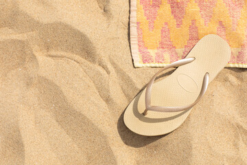 Fototapeta na wymiar Beach sand with a beige flip flop sandal and a vintage looking beach towel creating a mindful relaxing scenery in the summer sun. Holiday, tropical vacation concept