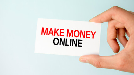 businessman's hand holding paper business card with text make money online, closeup light blue background