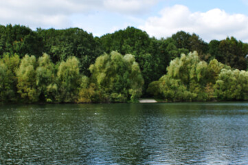 Blurred lake panorama background. Without focus, the water surface of the lake and the trees on the shore.