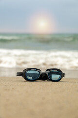 Fototapeta na wymiar goggles for swimming in the water placed on the sand on the shore of the beach in a sunny sunrise