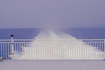view from the back of a large ship towards the sea with a white railing