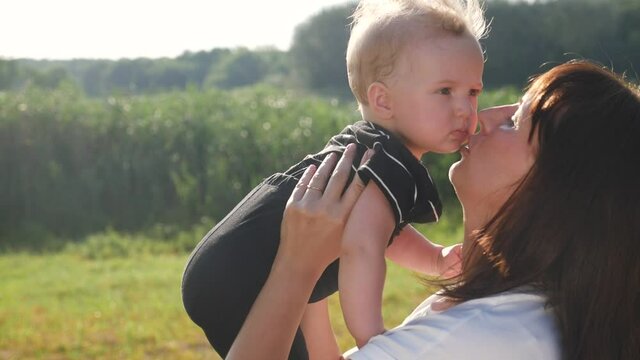 mom kiss newborn baby son holds in his arms playing in the park. mother day kid dream childhood happy family concept. parent play on hands with lifestyle a little boy son sunlight. people in the park