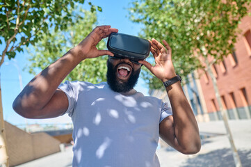 A dark-skinned man in a white tshirt in vr glasses looking excited