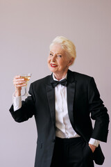 stylish mature sommelier senior woman in tuxedo with glass of sparkling wine. Fun, party, style, lifestyle, alcohol, celebration concept