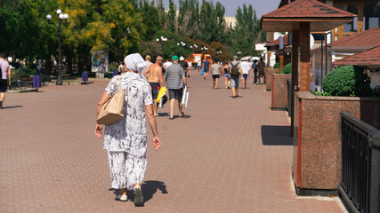 People walk along the wide embankment on a sunny day, in the foreground a mature woman walks forward