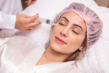 closeup of woman applying ozone to her face for cosmetic treatment. - obrazy, fototapety, plakaty