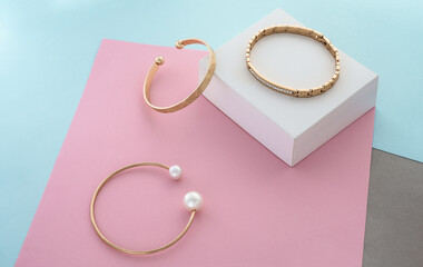 Three modern gold bracelets on pastel colors paper background with copy space