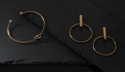 Fototapeta na wymiar Top view of Knot shape golden bracelet and earrings pair on black plates