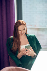 Cheerful woman with smartphone waiting for meeting in cafe