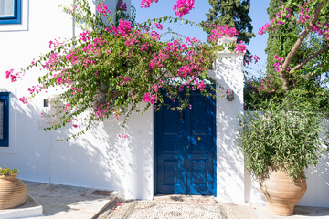Facade of a typical Greek white building with a blue door and blooming bougainvillea