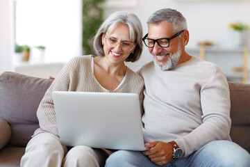 Happy senior family couple watching comedy or funny video on laptop while spending free time at home