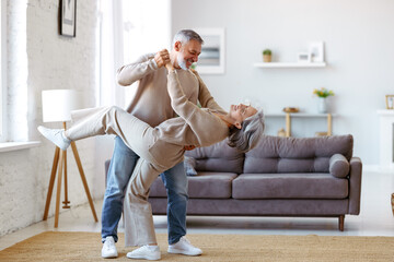 Romantic senior family couple wife and husband dancing to music together in living room