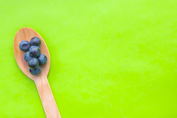 Flat lay of recycled spoon and juicy, fresh blueberries on color table. Space for text. Isolated ripe sweet bilberry fruits in eco spoon on green background. Copy Space. Healthy raw vegetarian food 