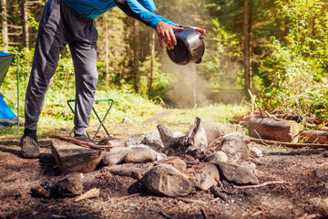 Man extinguishing campfire with water from cauldron in summer forest. Put out campfire. Traveling...