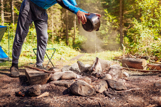 Man Extinguishing Campfire With Water From Cauldron In Summer Forest. Put Out Campfire. Traveling Fire Safety Rules