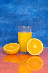 Glass of fresh orange juice with fresh fruits on blue background
