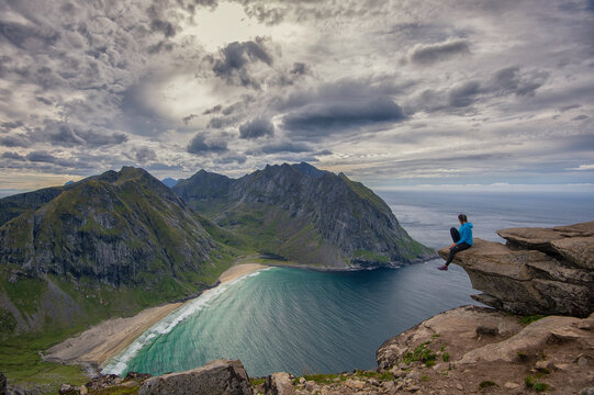 person sitting on a shelf of rock above the famous beaches "Kvalvika" and "Vesterrvika" in flakstad island, Lofoten