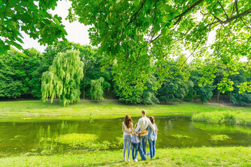 Fototapeta premium rear view of family embracing while standing near the lake. Parents with two children spend time outdoors.