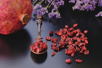 Ripe pomegranate and organic dry anardana or sun dried seeds of pomegranate fruit on dark background in vintage cooper oriental design spoon.Focus on foreground. Organic herbs and spices.