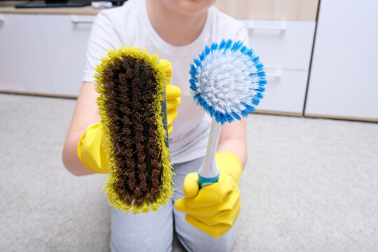 A child in yellow rubber gloves showing bruses for cleaning house, carpet from dust and stains