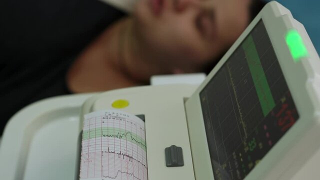 Young Pregnant Woman On Hospital Couch During Medical Control Cardiotocography. Visit Gynecologist Doctor At Clinic For Pregnancy Consultant. Examine Expectant Belly Baby Mother Healthcare Check Up