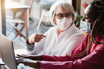 Diverse young and senior business people with protective masks working inside modern office - Focus on old woman face