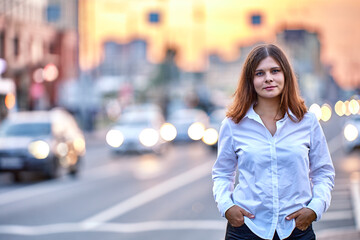 Young woman stands near traffic at summer evening.