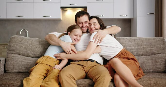 Happy parents and preteen daughter taking medical masks off and hugging cheerfully after coronavirus pandemic while sitting together on sofa at home