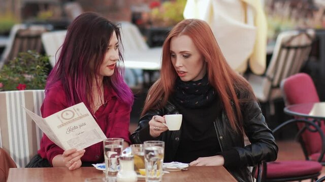 Two frends girls chatting in cafe using tablet pc. A cute Asian girl spends the summer on vacation in Europe. The girl is happy and enjoys life. A woman walks through the European streets. Friendship