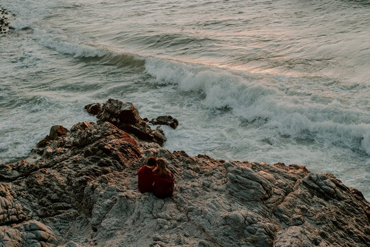 High angle shot of a couple sitting on cliffs near the sea