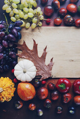 Seasonal composition with pumpkins, grapes, autumn leaves, ripe fruits and vegetables on rustic wooden board
