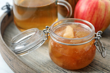 Delicious apple jam in jar on wooden tray, closeup
