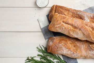 Delicious French baguettes and rosemary on beige wooden table, flat lay. Space for text