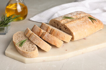 Cut delicious ciabatta with rosemary on white table