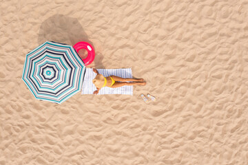 Fototapeta na wymiar Woman resting under striped beach umbrella at sandy coast, aerial view. Space for text