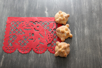 Papel picado tablecloth on wooden table as Mexican Day of the Dead decoration with delicious, fluffy and sugary bread of the dead

