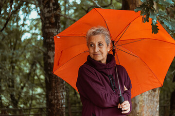 portrait of mature woman with gray hair  holding an orange umbrella on a rainy fall day.