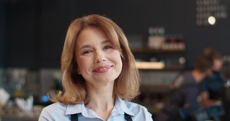 Close up portrait of happy cheerful middle-aged pretty woman looking at camera with smile on face in cafe. Beautiful joyful waitress smiling in own cafeteria at work, businesswoman concept