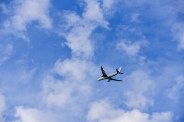 Passenger plane is flying far away against the blue summer sky with clouds