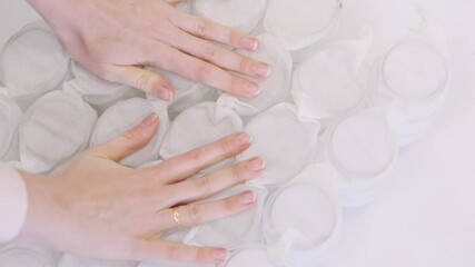 The girl presses on a mattress with large springs. Mattress test in a furniture store
