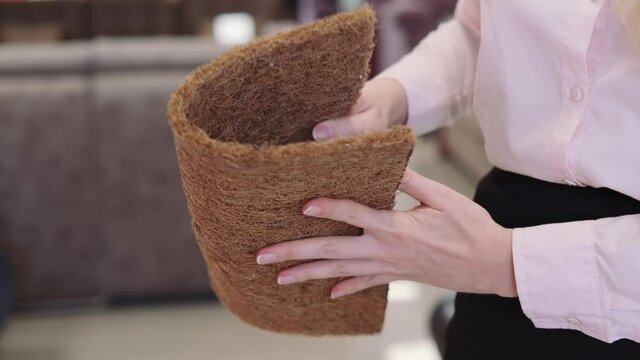 The girl squeezes a sample of coconut coir. Mattress material test in a furniture store
